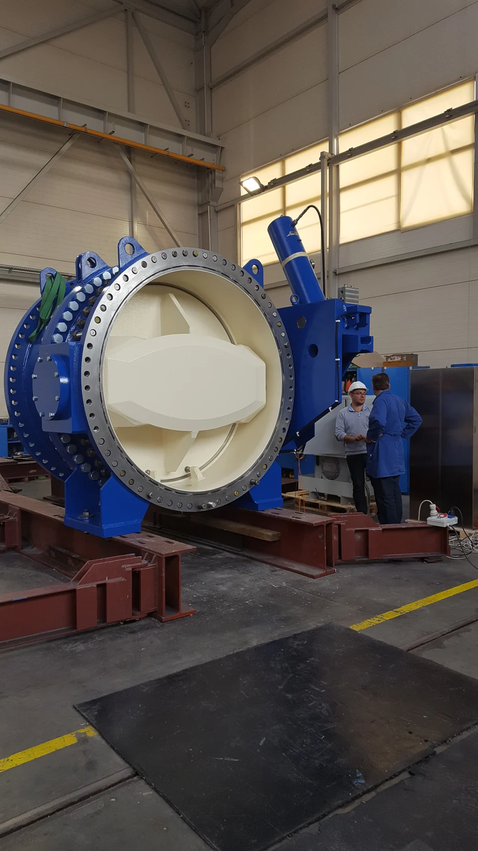 Large blue butterfly valve with two people beside it in a manufacturing facility
